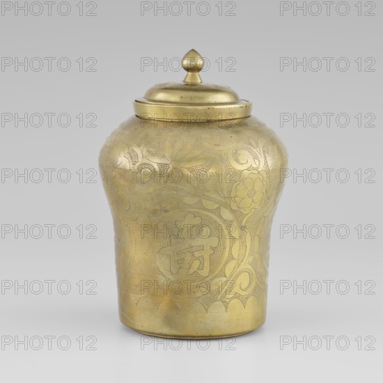 Tin with a lid; tin; early 20th century; Korean; container with widened top; height 15.0 cm; diameter 9.8 cm; decorated with peony plant ornament., A brass lidded jar with a rounded body and a domed lid topped by a teardrop-shaped finial fills the frame, showing an overall golden color with a slightly aged patina. The surface of the jar is decorated with incised floral and foliate patterns, including stylized flower motifs and curling vine-like designs, all rendered in the same golden tone with subtle variations in brightness where the metal is more polished or shaded. The jar has a gently scalloped border near the base and a smooth rim beneath the lid. The background is a neutral light gray, and the jar sits on a similarly light surface.