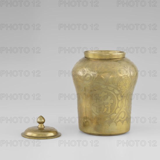 Tin with a lid; tin; plant ornament with peonies; Korean; early 20th century; container; height 15.0 cm, diameter 9.8 cm., A brass-colored metal jar with a rounded body and flared rim sits on a light neutral surface, accompanied by its separate lid placed nearby. The jar's exterior shows engraved floral and swirling decorative patterns covering much of its surface, with varied textures from smooth reflective areas to finely incised detailing. The lid is dome-shaped with a smooth knob finial and has a matching brass color and subtle engraved decoration. The background is a gradient of light gray tones. The visible colors are brass/golden, light gray, and subtle darker gray shadows.