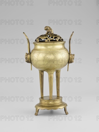 Censer with a cover, Censer with two long handles with mascarons. Decoration: two reserves — fruits and leafy twigs, animals and birds among trees. Early 20th century, Korea. Vessel censer. Height 15.0 cm; diameter 9.8 cm., A brass vessel with a rounded body stands on a raised circular base and a group of tall tripod legs; the body has incised decorative leaf and vine patterns and a warm golden color with areas of darker patina. Two curved vertical handles extend upward from opposite sides, each attached to a sculpted animal head in a similar golden tone. The lid is pierced with an openwork pattern and topped by a small sculpted animal figure, showing the same brass color and subtle shading. The base and legs show engraved decorative bands and the overall scene is set against a pale gray background.