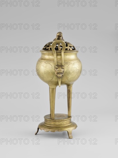 Censer with a cover, censer with two long handles with mascarons. Decoration: two reserves — fruits and leafy twigs, animals and birds among trees. Early 20th century, Korea; vessel, censer; height 15.0 cm, diameter 9.8 cm., A brass tripod censer with a domed pierced lid sits on a scalloped circular base; the censer body is bulbous with engraved decorative panels and a smooth rim, and it is supported by three long tapered legs connecting to a round platform above the base; a looped handle rises from the lid and a stylized animal head spout projects from the front; visible colors are brassy gold tones, muted brownish highlights, and a neutral light gray background.