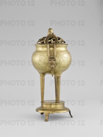 Censer with a cover, Censer with two long handles with mascarons. Decoration: two reserves—fruits and leafy twigs, animals and birds among trees. Early 20th century, Korea. Vessel censer. Height 15.0 cm; diameter 9.8 cm., A brass vessel with a domed, pierced lid sits elevated on a stand; the vessel is golden in color with a smooth, reflective surface and engraved decorative panels, and the lid has openwork patterns and a curved handle piece topped by a sculpted element. The body of the vessel is bulbous and rests on three tall, straight legs that connect to a round platform base with a scalloped outer edge and short curved feet; the legs and base share the same golden brass color and have subtle engraved motifs. A sculpted mask-like form is attached below the rim on the front of the vessel, and the overall scene shows the object centered against a soft gray background.