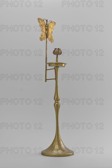 Candlestick, gift; decorated with butterflies and flowers; Korean; early 20th century; candlestick on a round base transitioning into a two-baluster shaft terminating in a flat, round sleeve with a smaller one in the shape of a multi-petaled flower bud placed in the center; one of a pair paired object no. SKAZsz 2509; height 39.7 cm., A tall metallic object with a narrow, elongated stem widening into a flared base, all in a golden brass color with engraved decorative patterns, topped by a shallow round dish and a stylized flower-like holder, and featuring a vertical rod extending upward that supports a decorative butterfly-shaped ornament in the same golden brass color; the background is a smooth light gray.