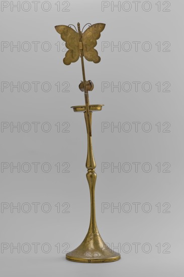 Candlestick, early 20th century, Korea; candlestick on a round base transitioning into a two-baluster shaft terminating in a flat, round sleeve with a smaller one in the shape of a multi-petaled flower bud placed in the center; decorated with butterflies and flowers; from a pair; height 39.7 cm., A tall metallic object with a slender, elongated stem and a flared, rounded base etched with decorative patterns, topped by a small shallow dish and a vertical rod that culminates in a butterfly-shaped ornament; the surface appears predominantly brass-colored with areas of darker patina and subtle variations in tone, set against a neutral light-gray background.