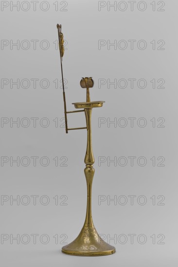 Candlestick, Early 20th century, Korea. Candlestick on a round base transitioning into a two-baluster shaft terminating in a flat, round sleeve with a smaller one in the shape of a multi-petaled flower bud placed in the center; ornamented with butterflies and flowers. From a pair other: no. SKAZsz 2509. Height 39.7 cm., A tall slender metallic stand with a flared round base and a long tapering stem rising to a small horizontal platform topped by a petal-shaped cup; a thin vertical rod with a decorative element extends upward from the platform area and is connected by a short horizontal brace. The object appears to be made of a golden-colored metal with subtle engraved patterns on the base and faint surface markings. The background is a smooth light gray. Colors visible include gold on the object and light gray in the background.