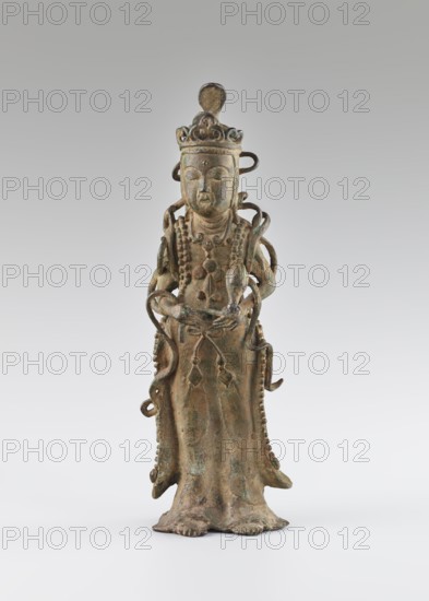 Guanyin, unknown creator;, figurine/sculpture; materials show natural patina; subject: Guanyin bodhisattva of mercy, goddess, Buddhist art, Chinese Buddhism; style/period: Ming 1368–1644, 16th century ; place of origin: China; height: 39.7 cm., A standing sculptural figure made of a brownish-green aged metal with visible verdigris, wearing a tall ornate headdress and layered jewelry, with a serene facial expression and closed eyes; the figure has flowing drapery that reaches the base, with looping decorative elements around the shoulders and arms, and a rounded top element above the head; the surface shows textured patina in tones of brown, green, and hints of bluish-green against a smooth pale gray to white gradient background.