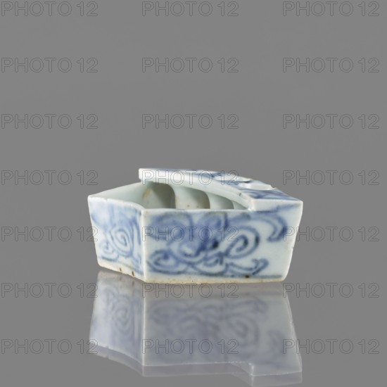 Vessel, gift, repossession Krakow, ceramics, Chinese art, Chinese culture, plant ornaments, blue-and-white porcelain, brick-red balls fired from clay, early 20th century, China, vessel; height 2.6 cm, width 7.4 cm, depth 4.7 cm., A small ceramic object sits on a reflective surface, showing a pale bluish-white base color with darker blue swirled brushwork on its outer faces; its shape is angular with a sloped top and an open compartment visible, and the piece shows subtle glazing highlights and a few small brownish spots on the interior edge, all set against a neutral gray background with the object’s reflection visible beneath it.