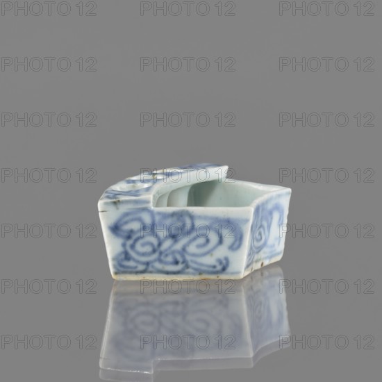 Vessel, gift, repossession Krakow, ceramics, Chinese art, Chinese culture, plant ornaments, blue and white porcelain, brick-red balls fired from clay, early 20th century, China, vessel, height 2.6 cm, width 7.4 cm, depth 4.7 cm, A small ceramic object with a rectangular shape and an open top, decorated with swirling painted patterns in blue on a white ground; the interior appears pale blue-green, the rim has a raised section with rounded indentations, and the base shows a slightly darker edge with a few small brownish spots; the piece sits on a reflective surface that mirrors its blue and white colors, and the background is a uniform gray.