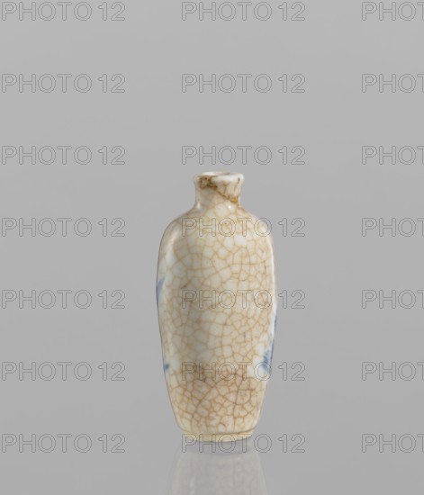 Flask–snuffbox, 19th century, China. Elongated ovoid flask with a narrow short neck; blue-and-white porcelain with bluish glaze and cracklework highlighted in brown paint; figural scenes. Function: snuffbox/vessel. Height 7.3 cm; diameter 3.5 cm., A small ceramic bottle with a narrow neck and rounded shoulders standing upright on a reflective surface, displaying a crackled glaze pattern in beige and light brown over a creamy white base with a few pale blue patches, set against a plain light gray background.