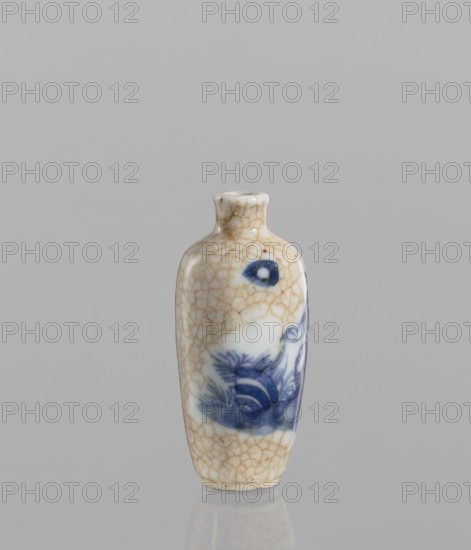 Flask — snuffbox; 19th century, China. Elongated ovoid shape with a narrow short neck; bluish glaze with cracklework highlighted with brown paint. Blue-and-white porcelain, figural scenes. Height 7.3 cm; diameter 3.5 cm., A small ceramic vessel with a narrow neck and rounded shoulders stands against a plain gray background; the surface shows a network of beige crackle lines over a white base, with areas of blue painted decoration including darker blue accents and a few pale blue washes, and the vessel casts a soft reflection on the smooth surface beneath it.