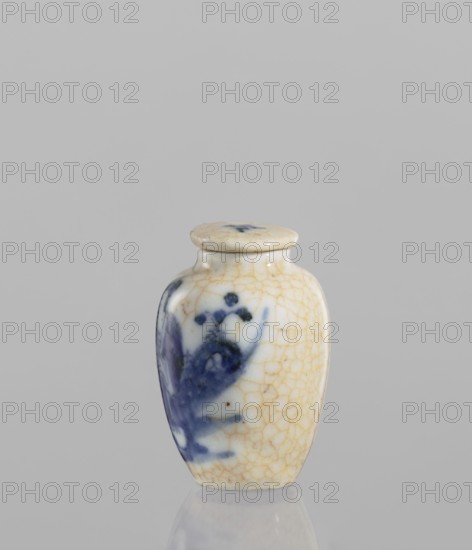 Flask - snuffbox with stopper, ceramics, Chinese, blue and white porcelain, figural scenes, cracklework decoration. The flask is short and wide with a short neck; cracklework embedded in yellow paint. The porcelain stopper is flat. The glaze is bluish, transparent, with minor impurities. Decoration is underglaze painted with cobalt. The stopper and flask are decorated with cracklework. 19th century, China, vessel; height 6 cm, diameter 4 cm., A small ceramic jar with a rounded body and a fitted lid sits against a plain gray background, showing a crackled off-white glaze with a pattern of fine tan crack lines and a painted blue floral or abstract motif on one side; the lid is similarly off-white with crackling and a small blue brushmark, and the jar's surface reflects slightly on the glossy surface beneath it.