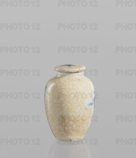 Flask - snuffbox with stopper, ceramics, Chinese, Chinese art, figural scenes, blue and white porcelain, cracklework decoration. The flask is short and wide, with a short neck, with cracklework embedded in yellow paint. The porcelain stopper is flat. The glaze is bluish, transparent, with minor impurities. The decoration is underglaze painted with cobalt. The stopper and flask are decorated with cracklework. 19th century, China, vessel; height 6 cm, diameter 4 cm., A small ceramic jar with a lid sits against a plain light gray background; the jar is off-white with a network of fine beige crackle lines across its surface and has a few spots of blue on its sides and top, with a glossy finish and a rounded, slightly tapered shape.
