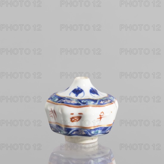 Spice vessel, 19th century China; blue-and-white porcelain vessel for spices no stopper, decorated with bats; height 4.65 cm, diameter 5.5 cm., A small porcelain object with a rounded, flared top and a scalloped body sits against a plain gray background; its surface is primarily white with decorative bands of deep blue and lighter blue wave-like patterns near the top and bottom edges, accented by thin gold or ochre lines; there are a few small reddish-orange brush marks on the body; the top has blue petal-like motifs and the piece rests on a short cylindrical white base that reflects faintly on the glossy surface below.