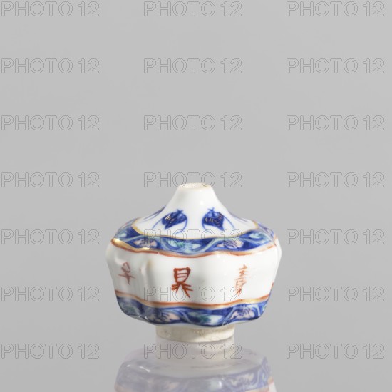 Spice vessel, gift, repossession, ceramics; blue-and-white porcelain; 19th century, China; subject: bats; function: spice vessel; no stopper; height 4.65 cm, diameter 5.5 cm., A small ceramic object with a rounded, fluted body and a short conical top, predominantly white with decorative bands and motifs in blue and accents of gold and reddish-brown; the upper and lower edges feature a blue wave-like pattern with touches of green, the top has blue floral or leaf-like motifs, and there are small reddish-brown marks on the white body; the piece sits on a short white base and is shown against a pale gray background with its reflection faintly visible.