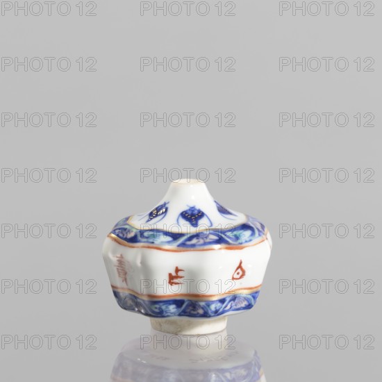 Spice vessel, ceramics, blue and white porcelain, 19th century, China; subject: bats; function: spice vessel No stopper; dimensions: height 4.65 cm, diameter 5.5 cm., A small white ceramic object with a rounded, flared shape sits against a light gray background, featuring decorative bands of blue and orange around its midsection and base, and blue floral-like motifs on the upper section; the piece has smooth glossy surfaces, a short central opening at the top, and a slightly irregular foot with a beige underside, and a reflection is visible beneath it.