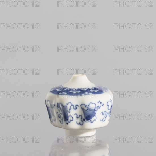 Small spice vessel, blue-and-white porcelain, 19th century China; no stopper. Height 4.6 cm, diameter 5.5 cm. Subject/ornament: hundred antiquities baigu., A small white ceramic object with a rounded, slightly flared top and a narrow circular base sits centered against a pale gray background; the surface of the object features a blue decorative band near the top and a repeating blue pattern around the middle consisting of abstract shapes and curved motifs, and the object and its base cast a soft reflection on the glossy surface beneath it.