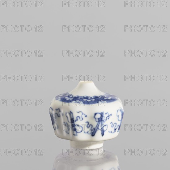 Small spice vessel, blue-and-white porcelain, 19th century China. Vessel no stopper, height 4.6 cm, diameter 5.5 cm., A small white porcelain object with blue painted decorative patterns sits against a light gray background, showing a rounded top with a short narrow neck and a wider flared body that has a scalloped profile; the blue decoration forms a band near the top with floral-like motifs and a series of abstract, curving line designs around the sides; the surface is glossy and reflects onto the smooth surface beneath it; visible colors include white, blue, and light gray.