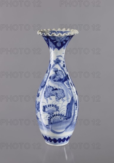 Vase, ceramics, blue and white porcelain, Japanese art, plant ornaments; 19th/20th century, Japan; vessel; height 36.6 cm, diameter 14 cm, A slender ceramic vase with a flared, ruffled rim stands against a plain background; the vase is predominantly white with blue decorative painting all over its body, including floral and botanical motifs and flowing brushwork that create curved and rounded shapes; the rim shows alternating scalloped edges with blue accents, and the lower section displays a band of darker blue patterns above the base; visible colors in the image include shades of blue, white, and the neutral gray of the background.