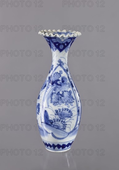 Vase, ceramics; blue and white porcelain vase with plant ornament; Japanese, 19th/20th century; vessel; height 36.6 cm, diameter 14 cm., A tall ceramic vase with a ruffled rim, predominantly white with blue painted floral and decorative motifs, showing a narrow neck that flares to a scalloped mouth and a bulbous body tapering to a small base; the blue designs include stylized flowers and leafy patterns arranged in panels and bands, with darker blue accents near the rim and base, all set against a smooth neutral gray background.
