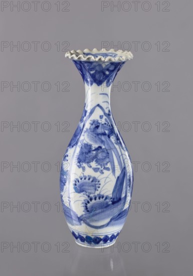 Vase, ceramics, blue and white porcelain, Japanese, 19th/20th century Japan; vessel with plant ornaments; height 36.6 cm, diameter 14 cm., A porcelain vase with a flared, ruffled rim sits against a plain gray background, the vase predominantly white with blue painted floral and foliage motifs covering its elongated, curving body and narrowing neck, showing brushstroke textures and areas of deep and lighter blue, with a decorative blue band near the base and a glossy surface that reflects light.