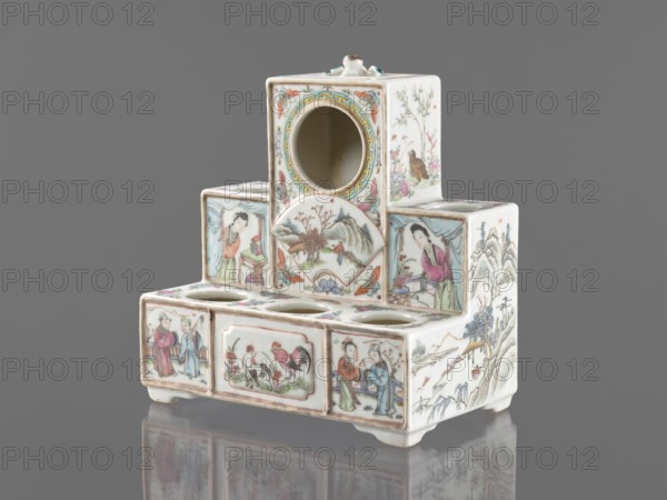 Pedestal for a writing set three-stage, gift, repossession Krakow, ceramics decorated with flowers, figural scenes, butterflies and landscape motifs in colored porcelain, Qing style late 19th century, Qing 1644–1911, Chinese, raised central part, writing accessories, height 18.9 cm, width 17.9 cm, depth 11.0 cm, A small multi-tiered ceramic object with a glossy white base decorated in painted scenes and floral motifs in colors including pink, green, blue, brown, yellow, and black. The piece has a stepped rectangular form with a circular opening near the top and several circular recesses on a lower tier. Painted panels show human figures wearing traditional clothing, birds, roosters, and landscape elements such as mountains, trees, and rocks. Delicate floral decorations and patterned borders appear around the openings and panels. The object sits on short feet and is photographed against a neutral gray background with a soft reflection visible beneath it.