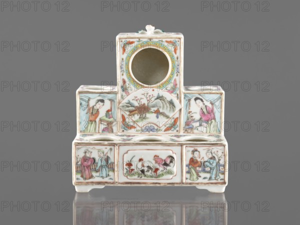 Pedestal for a writing set three-stage, colored porcelain, late 19th century, China; Qing style Qing, 1644–1911. Decorated with ceramics flowers, butterflies, landscape motifs and figural scenes; raised central part. Function: writing accessories. Dimensions: height 18.9 cm; width 17.9 cm; depth 11.0 cm., A small ceramic object with a stepped rectangular form sits against a gray background, predominantly white with painted decoration in colors including pink, green, blue, yellow, orange, brown, and black. The piece has a central circular opening near the top and a few round openings along the midline, and is supported by short feet. Painted panels on the front and sides depict several human figures wearing flowing robes in pink, green, blue, and red tones, scenes of people interacting, and a pair of roosters amid grass and flowers. Other panels show a landscape with trees and hills and decorative floral and butterfly motifs in pastel shades. The painted outlines and details are rendere...