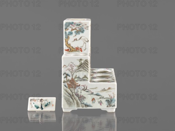 Pedestal for a writing set three-stage, late 19th century, China. Colored porcelain with raised central part; height 18.9 cm, width 17.9 cm, depth 11.0 cm. Decoration: ceramics with flowers, figural scenes, butterflies, landscape motifs in Qing style Qing, 1644–1911. Function: writing accessories., A small ceramic stepped object and a separate rectangular ceramic lid sit on a reflective surface against a plain gray background; the stepped piece is primarily white with painted scenes in colors including blue, green, brown, red, pink, and black, showing landscape elements like trees, mountains, and small human figures, as well as a bird near a tree on the upper section; the top face of the lower step has three circular openings; the rectangular lid is white with a small raised decorative element painted in green and brown and also reflects faintly on the surface.