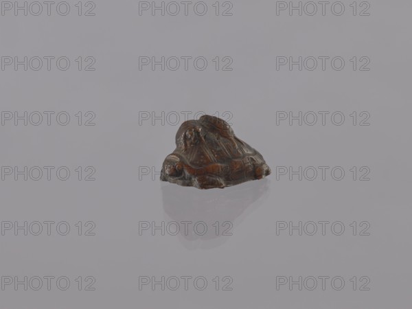 Group of turtles; okimono; creator, ceramicist; ; Japanese; Meiji 1868–1912, 19th/20th century; figurine; height 2.8 cm, width 3.5 cm, depth 5.5 cm, A small carved object sits on a smooth reflective surface, showing a glossy dark brown with areas of lighter brown and black; the object has an irregular rounded shape with carved ridges and contours, and a subtle mirrored reflection beneath it; the background is a uniform pale gray.
