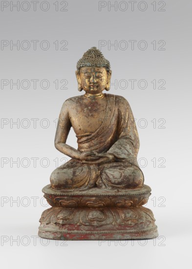 Buddha, unknown sculptor, Chinese, Qing dynasty 1644–1911, 18th century, sculpture; figurine of Buddha with ushnisha seated on a lotus throne; materials not specified; height 25.5 cm, width 16.0 cm; Buddhist art, Chinese Buddhism, lotus throne iconography, Buddha iconography., A seated statue of a figure on a tiered lotus base, shown frontally, with a textured hair surface and elongated earlobes; the figure wears a draped robe over one shoulder and has hands resting in its lap in a meditative gesture. The surface shows worn areas and peeling finishes, revealing metallic tones and patina. Visible colors include gold, greenish-blue, brown, reddish accents, and grey.