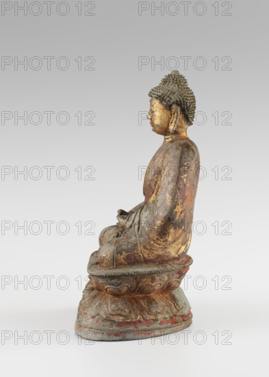Buddha, gift, Chinese, Qing 1644–1911, Buddhist art, Chinese Buddhism, Buddha iconography with ushnisha, lotus throne iconography, figurine sculpture, 18th century, height 25.5 cm, width 16.0 cm, A seated statue of a figure shown in profile facing left, with a textured hair or headpiece, a calm facial expression, and elongated earlobes. The figure wears a draped garment and sits on a rounded, lotus-like pedestal with carved petal shapes. The surface shows worn and flaking finishes revealing metallic gold, greenish patina, brown, reddish accents, and areas of gray. The background is a smooth gradient of pale gray to off-white.