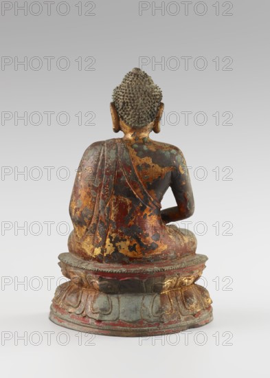 Buddha, Qing dynasty 1644–1911, 18th century, China, Chinese Buddhist art; sculpture/figurine of Buddha with ushnisha on a lotus throne; height 25.5 cm, width 16.0 cm., A rear view of a seated statue on a rounded pedestal, showing a figure with textured, tightly curled hair and elongated ears; the figure wears a draped garment that covers one shoulder and cascades down the back, with visible wear and flaking revealing underlying layers. The surface shows a mix of colors including gold, dark brown, reddish tones, greenish patches, and areas of black, with the pedestal displaying muted green, red, and gold accents and worn edges. The background is a smooth gradient of light gray transitioning to slightly darker gray toward the top.