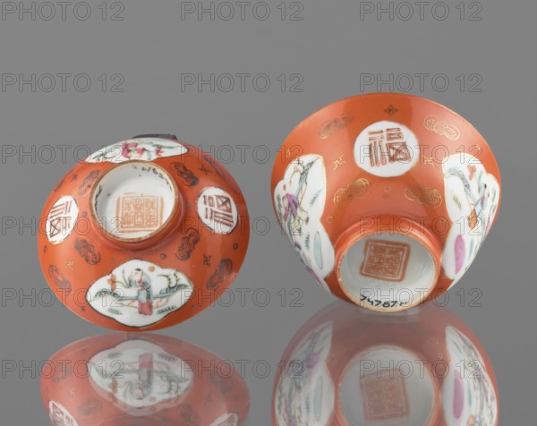 Bowl with a lid, attributed to an, Qing dynasty Tongzhi, 1862–1874, Chinese, colored porcelain. Decoration includes loosely placed bats and swastikas in the background and genre scenes. Vessel, height 8.6 cm, diameter 10.3 cm., Two small bowls rest on a reflective surface, showing their undersides. The bowls are primarily orange with white oval panels painted with scenes of people and foliage in colors including green, pink, purple, and blue. There are gold decorative motifs and small dark line details on the orange areas. The reflective surface beneath them creates mirror images of the bowls. The background is gray.