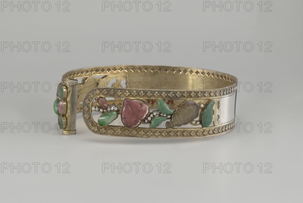 Headband, plant ornament, Chinese, Chinese art, Qing 1644–1911, head ornament, openwork inlaid with glass, semi-precious stones, river pearls and beads, 19th century, China, height 3.3 cm, diameter 12 cm., An ornate metal bracelet with a gold-toned band and decorative edging, featuring an openwork central panel set with polished stones and carved elements in shades of green and pink, along with small bead-like accents in a pearly white; the metal shows areas of a silvery tone and warm brass-like gold, and the piece rests on a neutral light-gray surface against a pale gray background.