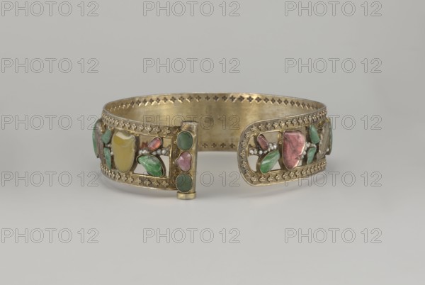 Headband; Openwork inlaid with glass, semi-precious stones, river pearls and beads; plant ornament; Chinese; Qing 1644–1911; 19th century; height 3.3 cm, diameter 12 cm., A decorative metal bracelet with a gold tone rests on a light gray surface against a pale gray background, featuring openwork panels set with a few polished stones in green, pink, red, and yellow, small bead-like accents in white, and ornate stamped border patterns; the bracelet has a hinge-like clasp area at the front and shows interior metal with a slightly darker gold patina.