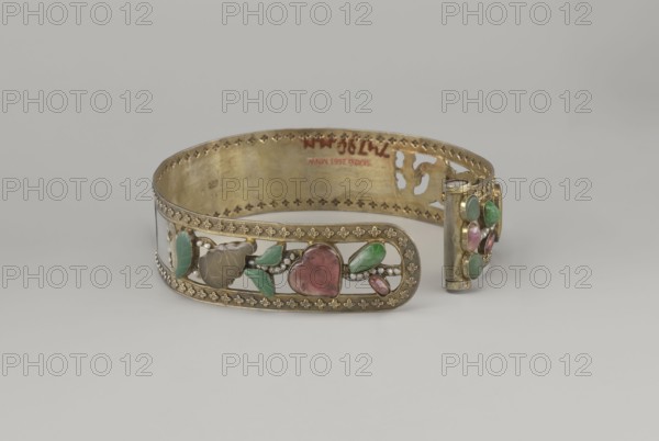 Headband, plant ornament, Chinese, Chinese art, Qing 1644–1911, head ornament, openwork inlaid with glass, semi-precious stones, river pearls and beads, 19th century, China, height 3.3 cm, diameter 12 cm., A decorative metal bracelet band with an openwork design rests on a neutral pale gray surface against a light gray background; the band is primarily gold-toned with a patterned border and ornate cutouts, and it features several inlaid stones and carved elements in green, pink, and pale gray, as well as small white bead-like accents; one end shows a cylindrical clasp element adorned with more green and pink stones, while the interior of the band reveals the same gold tone and decorative perforations.