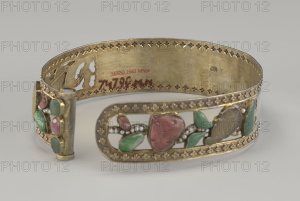 Headband, Chinese, Qing dynasty 1644–1911, 19th century. Openwork head ornament inlaid with glass, semi-precious stones, river pearls and beads; plant ornament. Height 3.3 cm, diameter 12 cm.,  noted., A decorative metal bracelet with a gold-colored finish is shown resting on a pale surface, featuring an open cuff design with ornate punched edging along its top and bottom rims; the outer face displays a series of floral and leaf motifs set into openwork panels with polished stone-like insets in shades of green and pink and small rounded bead accents in a pearly white, while the inner band shows the same gold-colored metal with signs of wear.