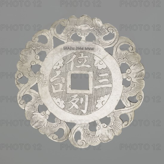 Pendant - amulet of good fortune; maker, Chinese; 19th century; materials/technique: decoration; imagery: bats; diameter 5.8 cm., A round ornamental object with a central square hole, made of a metallic material in shades of silver and grey, featuring an intricately pierced outer rim with a repeating floral or cloud-like pattern and scalloped edges, a textured inner ring with fine dotted engraving, and raised smooth bands separating the central design from the decorative border.