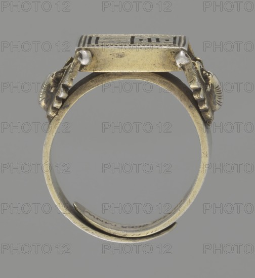 Ring, gift, Chinese, Chinese art, Jagniatkowska, Magdalena 1866–1944, Jagniatkowski, Wladyslaw 1856–1930, Qing 1644–1911, body ornaments, jewelry, hand ornaments, bats iconography, Shield with ideographic signs supported by two bats, 19th century, China, jewelry, dia. 2 cm, A metal ring shown from the side against a gray background, with a square decorative top held by a band that curves into a circular shank; the ring is mostly gold-toned with areas of darker patina and small silver-toned accents at connection points, and it features ornate carved or embossed elements on the sides near the top with textured scalloped and shell-like forms.