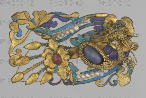 Fragment of a female head ornament, Chinese, Qing dynasty 1644–1911, 19th century. Materials: kingfisher feather and other jewelry materials. Motifs: phoenixes and ornamental designs. Function: female head ornament/jewelry. Dimensions: height 7.0 cm, width 4.4 cm. Creator: unknown., The image shows an ornate decorative object with a predominantly gold surface accented by areas of blue and turquoise enamel and several white pearls; there is a central oval cabochon in deep blue set in a textured gold bezel, a smaller rounded stone in red surrounded by gold petal shapes, and stylized gold floral and leaf forms extending outward; ribbon-like bands in blue and turquoise weave through the design, and there are several curved gold filigree elements and scrolls, all presented against a neutral gray background.