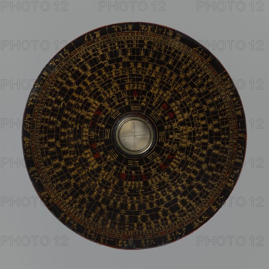 Feng shui compass luopan, Chinese, Qing 1644–1911, 19th century. San Yuan Luo Pan also known as yi pan or jiang pan containing the ring for the 64 hexagrams of the I Ching and a 24-direction ring; used by practitioners of the Three Cycles System of Feng Shui including Flying Stars Time Space. Materials/format: navigational/astrological measuring instrument compass, diameter 17.0 cm. Subjects/themes: astrology, calendars, Chinese Zodiac., A round, flat object viewed from above with concentric circular patterns and a central raised circular element resembling a glass-covered disk; the main surface is dark brown to black with a complex arrangement of thin lines and small markings in gold and occasional small areas of red, the outer rim showing a slightly worn edge with hints of reddish-brown, and the background is a uniform light gray.