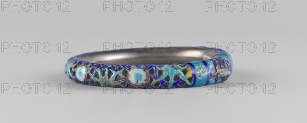 Bracelet, ; ornament, Chinese art, Chinese culture; women's ornament; Qing dynasty 1644–1911; 19th century; hundred antiquities baigu ornament; jewelry; diameter 11.0 cm., A circular metal bracelet sits on a light gray background, showing an ornate outer surface with openwork patterns and enamel inlays. The bracelet's interior is smooth and silvery-gray, while the exterior features a mix of blue tones including bright turquoise, deep royal blue, and pale sky blue, along with touches of dark gray and muted gold. The decorative surface includes floral and geometric motifs created by the enamel work and metal lattice, and areas where the enamel forms rounded, flower-like shapes and petal patterns. The piece appears slightly worn in places, with variations in the enamel's saturation and small areas where the underlying metal shows through.