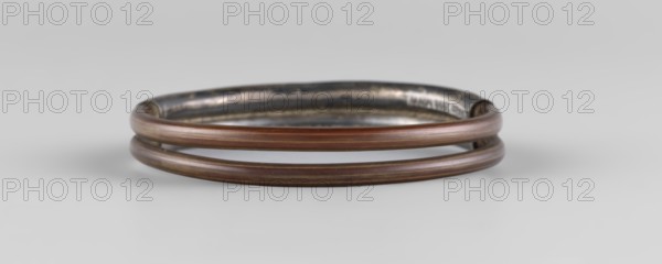 Bracelet, ; women's ornament, Chinese, Qing 1644–1911, 19th century; materials: enamel colors: white, yellow, teal, blue; motif: plant ornament; jewelry; diameter 7.0 cm., The image shows a circular, double-band bracelet resting on a smooth, light gray surface, with the bands appearing made of a brownish material with subtle reddish and golden tones; the inner rim of the bracelet has a darker, metallic gray appearance with some reflective highlights, and the overall scene has soft, diffuse lighting casting a faint shadow beneath the bracelet.