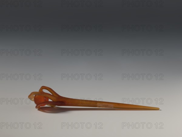 Hairpin, repossession Kraków - collection, Chinese art, Chinese culture, head ornament, women's ornament, toiletries, Qing 1644–1911, transparent amber, 17th–18th century, China, jewelry, length 13.6 cm, A single amber-colored hairpin lies horizontally on a smooth surface, with a glossy rounded bead near one end held by a curving, ribbed loop; the hairpin and loop are various shades of amber and orange with translucent and slightly darker accents, and the surface and background show gradients of gray and off-white.