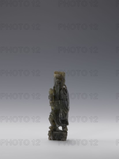 Sage; sculptor,  noted; figurines; Chinese; Chinese art; sages; Qing dynasty 1644–1911; grey-green soapstone; 19th century; China; sculpture; height 13.8 cm; width 4.4 cm; depth 3.1 cm, A small carved figurine stands on a rounded base, displaying a figure wearing a long robe and a rectangular hat, with a long beard and a contemplative expression; the sculpture shows flowing drapery folds and a hand holding a short object close to the chest, and the surface appears smooth and slightly glossy with visible tool marks. The colors visible are dark green, olive, and gray, with lighter greenish-yellow highlights and subtle brownish tones on areas of the hat and base, set against a neutral gray gradient background.