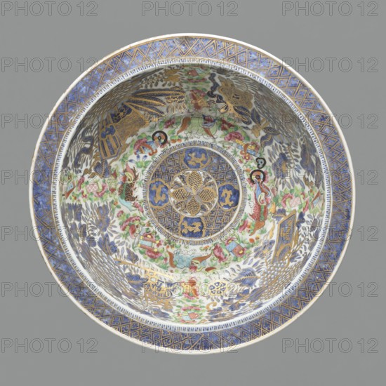 Bowl, famille rose porcelain, decorated with geometric ornaments, writing scrolls, lions, peonies, flowers, and the Eight Auspicious Signs; 19th century China; diameter 42.5 cm., A decorative shallow bowl is shown from above with an ornate interior featuring a central circular medallion surrounded by concentric bands of patterned decoration; the rim has a geometric border in blue and gold, and the interior area displays a busy design of floral and foliate motifs, stylized birds and animals, and small decorative objects rendered in colors including blue, gold, green, pink, red, and white, with fine linework and gilt accents throughout.