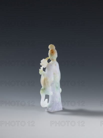 Taoist goddess?, Chinese, Qing 1644–1911, 2nd half of the 18th century, Taoism; figurine sculpture of a goddess holding a scepter, floral iconography; green-pink slightly translucent jade; height 17.1 cm., A small carved figurine of a standing person rendered in a smooth, translucent material with a polished surface, showing colors of pale white, light green, soft lavender, and warm amber; the figure wears flowing robes and has hair styled in a topknot, holds a long-stemmed flower near the face with one hand while the other hand rests by the side, and a portion of the lower garment forms a curved, openwork shape; the object casts a soft shadow on the neutral gray surface beneath and is set against a gradient dark gray to lighter gray background.