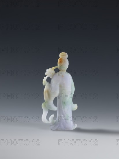 Taoist goddess?, Chinese, Qing 1644–1911, 2nd half of the 18th century. Green-pink slightly translucent jade figurine sculpture of a goddess with flowers and scepters, height 17.1 cm., A carved figurine of a standing person viewed from behind, made of a smooth, translucent stone showing pale green, lavender, white, and warm amber tones; the figure has a high bun hairstyle with amber coloring, flowing robes with soft folds and subtle green and lavender veining, and an extended arm holding a stylized flower-like object; the base of the figurine casts a soft shadow on a light grey surface against a dark grey to nearly black gradient background.