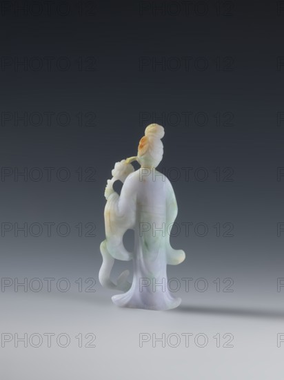 Taoist goddess?;, Chinese; Qing dynasty 1644–1911; Taoism; flowers iconography; scepter; green-pink slightly translucent jade; 2nd half of the 18th century; figurine sculpture; height 17.1 cm, A small carved figurine of a robed person seen from behind, standing on a flat surface against a dark gray to light gray gradient background, rendered in pale colors including white, light green, light purple, and touches of orange; the figure has a high hairstyle and holds a curved object with floral-like details, with flowing sleeves and a flared hem creating soft, rounded shapes and subtle shadowing on the surface beneath.