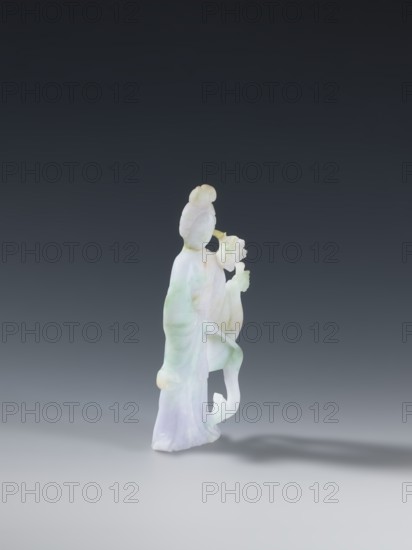 Taoist goddess?;, Chinese; Chinese art; goddesses; Qing dynasty 1644–1911; Taoism; iconography: flowers, scepters; material: green-pink jade, slightly translucent; 2nd half of the 18th century; place of origin: China; type: figurine, sculpture; height: 17.1 cm; provenance: purchase., A carved translucent figure standing on a smooth surface against a dark gray to black gradient background, rendered in pale white with areas of light green and faint lavender hues; the figure wears flowing robes with draped folds, has a rounded head with a coiled topknot, and holds a floral element near where hands would be, with graceful curved lines and soft shadow cast to the right.