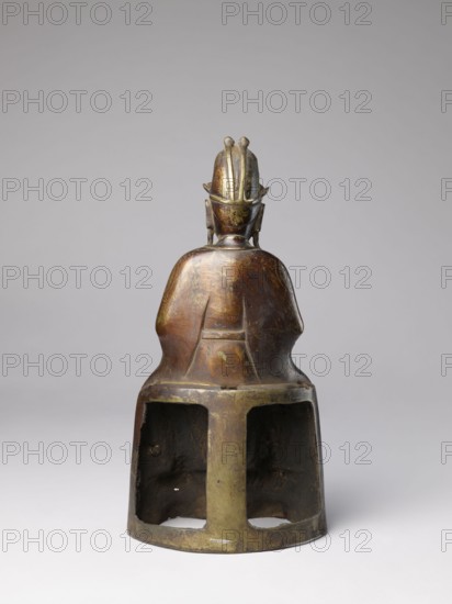 Mythical emperor, gift, Chinese art, Chinese culture, Qing 1644–1911, Qing style, figurine of a ruler in dragon robe with dragon iconography, 19th century, China, sculpture, height 41.0 cm, A bronze-colored sculptural figure shown from behind sitting on a hollowed base, with visible greenish patina and darker brown areas; the figure wears a rounded headpiece with vertical ridges and small protrusions, and has ear-like shapes at the sides; the upper back and shoulders are smooth and rounded, showing wear and mottled coloring in bronze, green, and dark brown; the base is ring-shaped with two open rectangular cavities revealing a darker interior and uneven surfaces, and the background is a neutral pale gray.