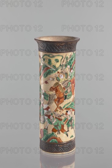 Vase, Chang author's role classification, workshop author. Flared rim. Cracked iron-sand glaze. Decorated with a scene of a knightly procession in a landscape a mirror equivalent of the decoration on the second vase in the pair. At the foot and at the rim, a band imitating a bronze representation. Knightly scenes, figural scenes, warriors. Ceramics; cylindrical vessel. 19th century. China. Height 31 cm; diameter 12 cm., A cylindrical vase with a flared rim and a raised base, decorated all around with detailed painted scenes showing a group of human figures in dynamic poses and several horses, set among stylized hills and foliage; the painted areas use green, brown, beige, red, black, and touches of white, while the rim and base have a textured darker brown band with carved wave-like patterns.